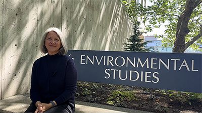 Dean Teena Gabrielson sits in front of the Environmental Studies building sign.