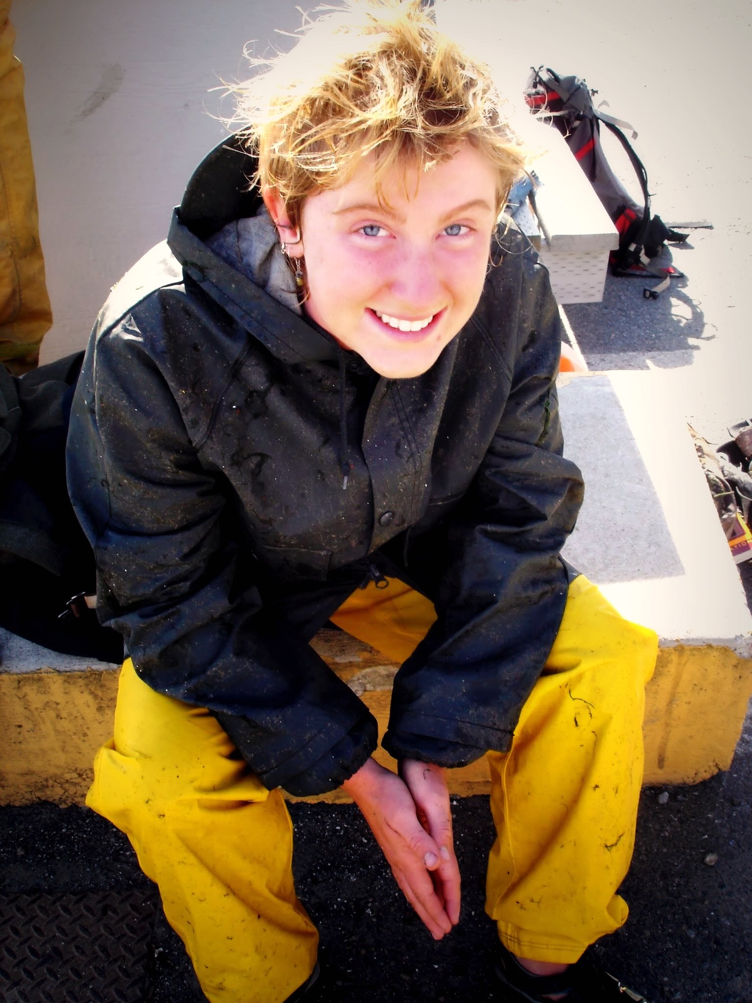 student wears waterproof pants and sits on the edge of a boat smiling