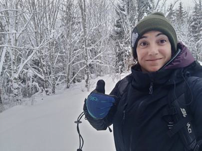 Dana Bronstein gives a thumbs-up, wearing cold weather gear in a snowy landscape.