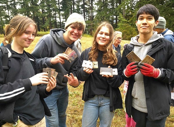 Four students stand holding up the cassette tapes they found while clearing brush in the Arboretum.