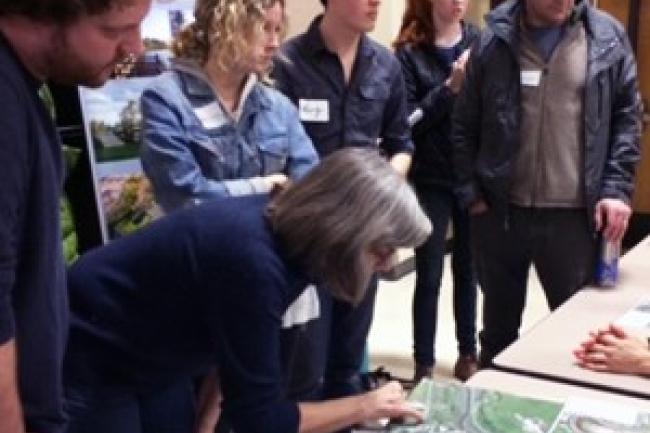 A group of Urban Planning students stand gathered around a large map placed on a table. 