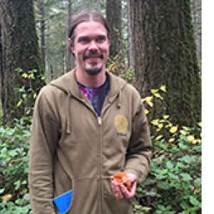 Tristan Woodsmith in the woods holding an orange mushroom