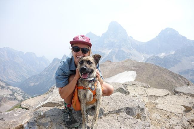 Kenna Kuhn poses with a dog on top of a mountain.