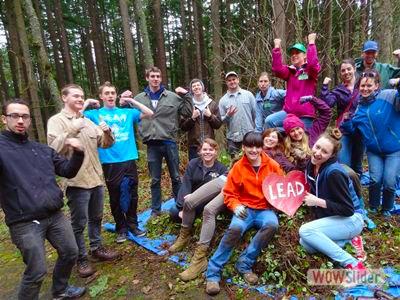 Group of LEAD volunteers gather in the forest over a pile of weeds that are stacked on a tarp.