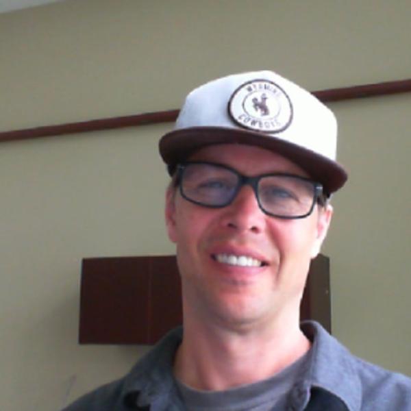 Tyson smiling at the camera in a white baseball hat and black glasses