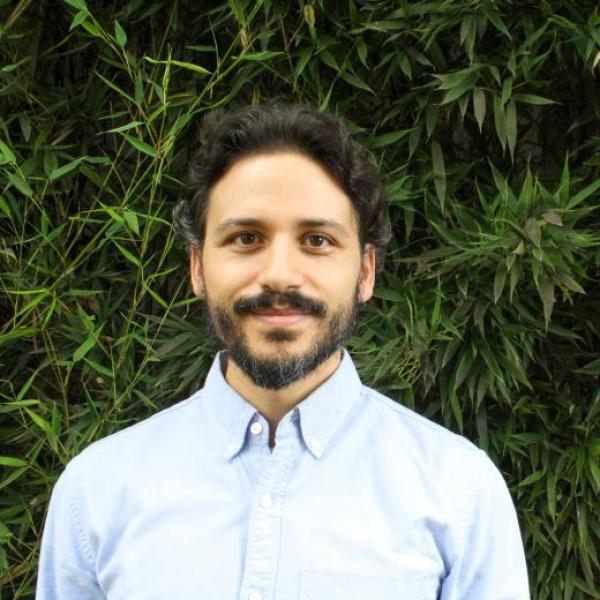 Francisco in a light blue button up shirt in front of a leaf background.