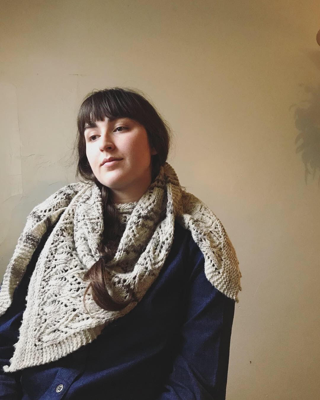 Portrait of Caroline Vogl sitting in front of a beige wall, wearing a blue button-down top and knitted, off-white scarf