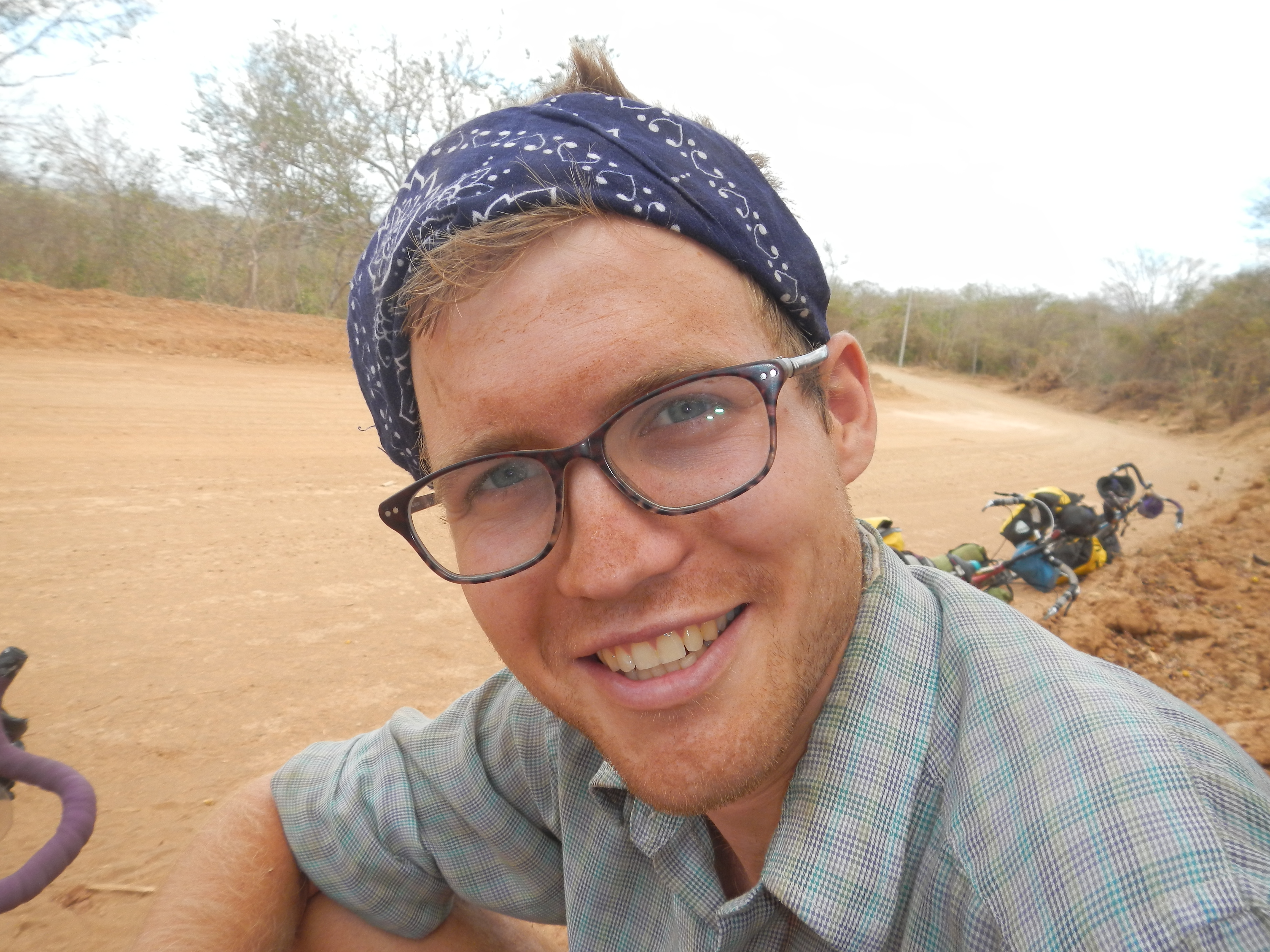 Close up portrait of Ventres-Pake smiling at the camera wearing a blue bandana as a headband and brown tortoiseshell glasses
