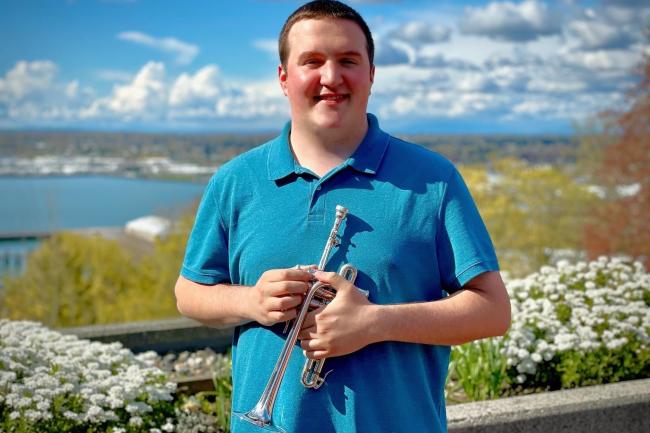 Alex Marbach holds a trumpet while standing on the PAC plaza