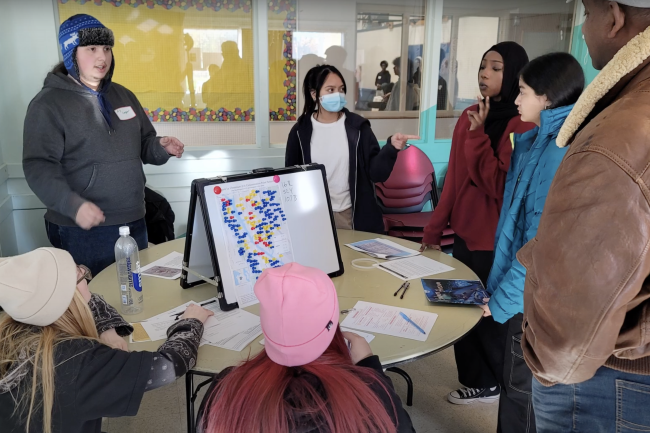 Screenshot of Environmental Justice Video phase 2 submission from Western, shows people gathered around a table discussing a graph