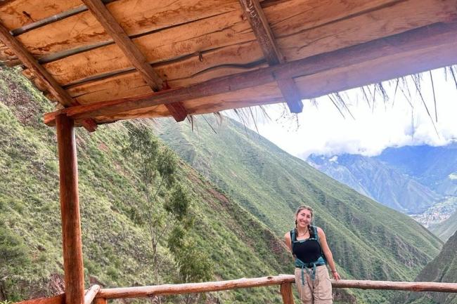 a student smiles at the camera in a shelter high in a lush green valley