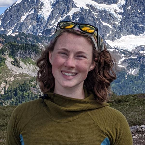 A student in a long sleeve shirt with sunglasses on their head standing in front of a mountain